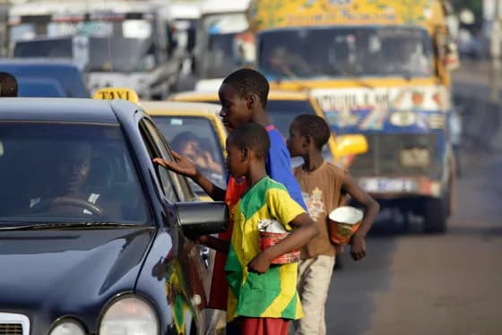 Children holding bowls beside cars in traffic.